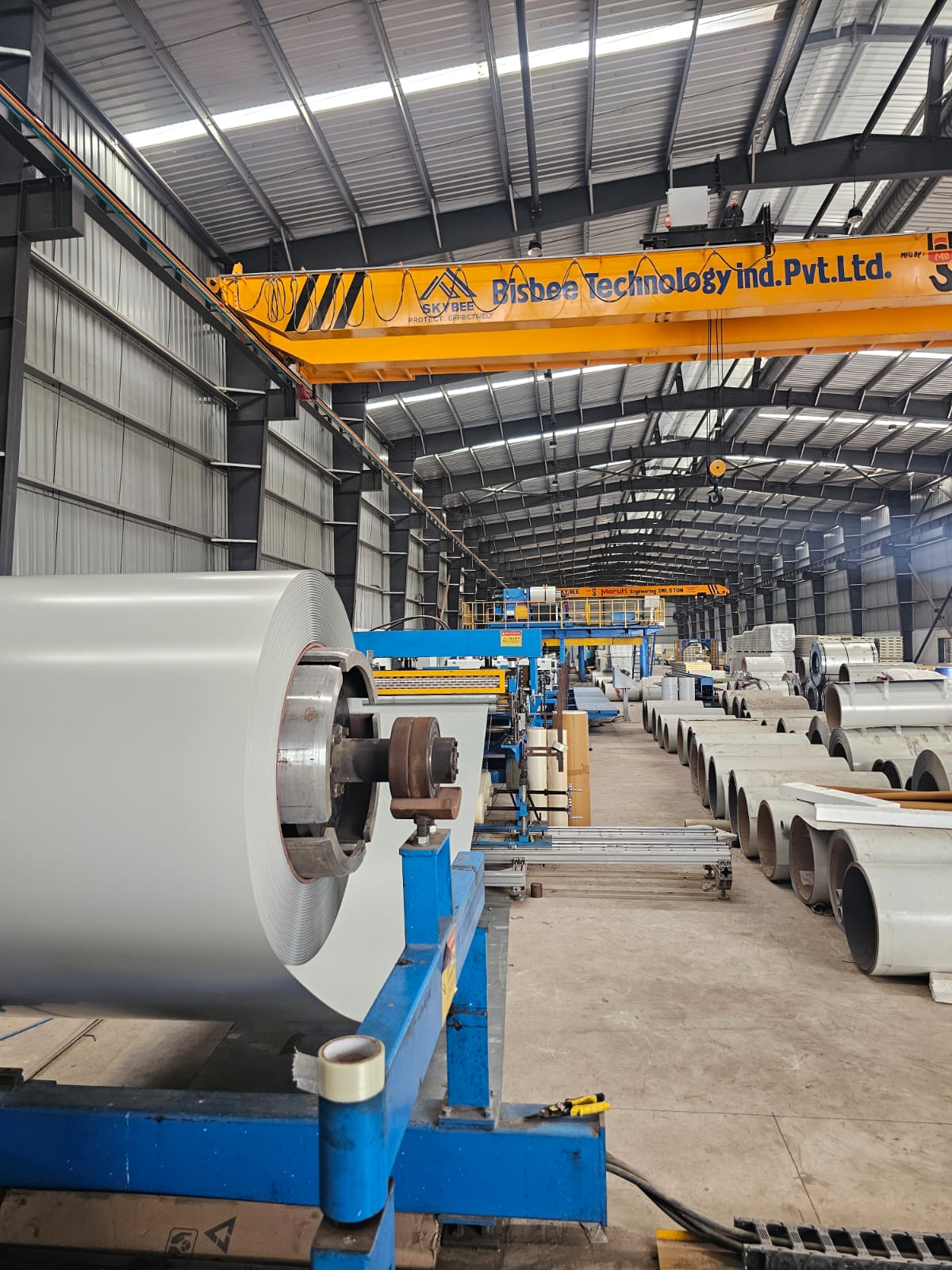Pre-painted steel coil mounted on automated production line uncoiler beneath overhead crane